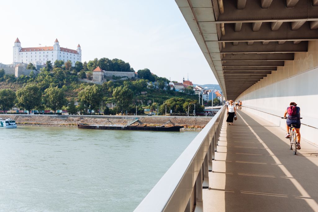 Cyclist on the pedestrian lane of the SNP (UFO) Bridge with Bratislava Castle above the Danube River – Slovakia Danube cycle path